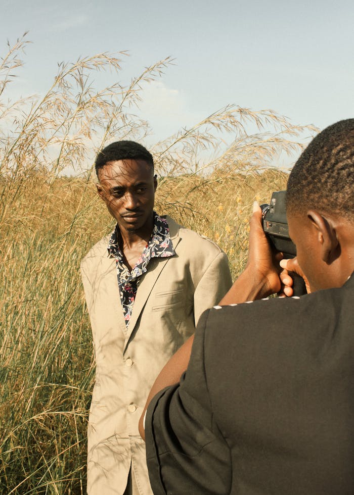 A stylish outdoor photoshoot featuring a model in tall grass with a photographer.
