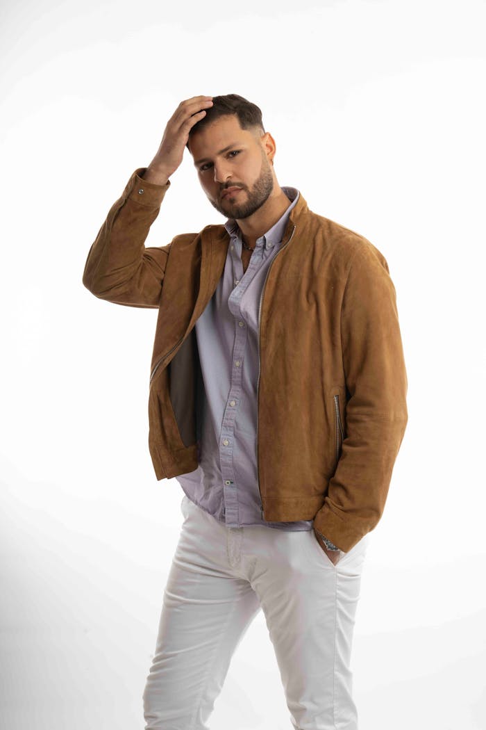 gallery-6 Confident young man posing in a suede jacket against a plain background.